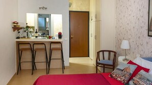 A hotel room with a bed, a desk with chairs, a chair, a lamp, and a door. - Old Bridge Apartment (Firenze)