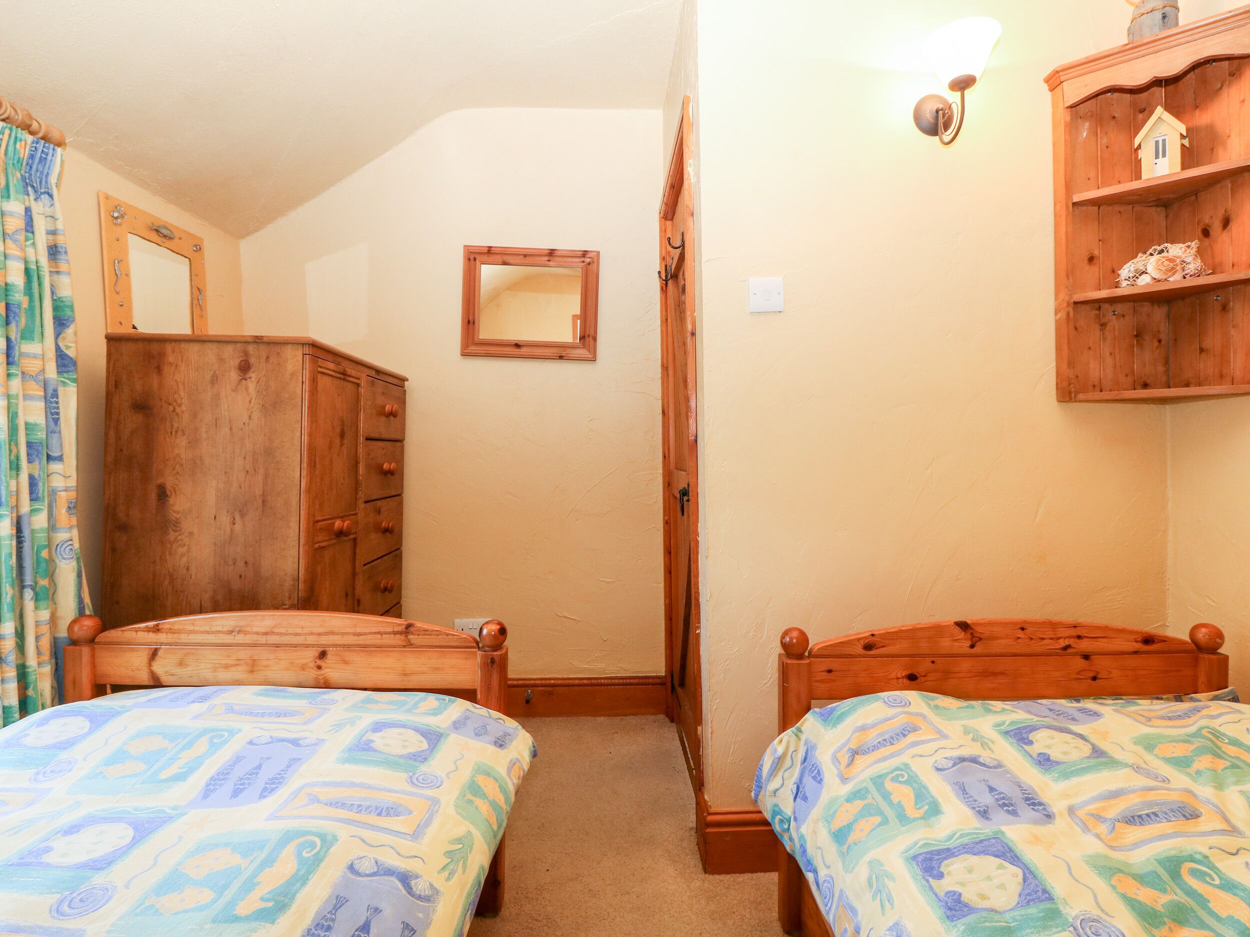 A bedroom with two wooden beds, a wooden wardrobe, a mirror, and a shelf with decorative items.