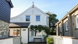 A narrow stone-paved courtyard with a white building featuring two windows and a small bench. - The Cottage (Pwllheli)