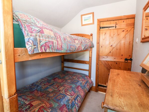 A bunk bed with a colorful patterned bedspread, a wooden door, and a small table. - The Cottage (Pwllheli)