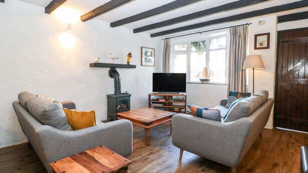 A cozy living room with a fireplace, comfortable seating, a television, and a wooden floor. - The Cottage (Pwllheli)