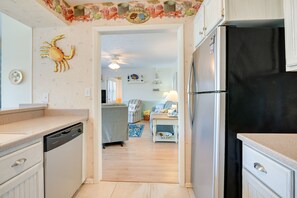 Relax in this open-plan living space featuring a kitchen with a dishwasher and refrigerator, a cozy sofa, and a decorative mural.