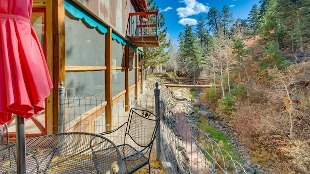 A wooden building with a balcony, a metal chair, and a red umbrella. - Riverside Retreat w/ Screened Porch: 6 Mi to Taos! (Taos)