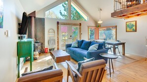 A spacious living area with a high ceiling, a wooden dining table, a blue sofa, and a wooden bench. - Riverside Retreat w/ Screened Porch: 6 Mi to Taos! (Taos)