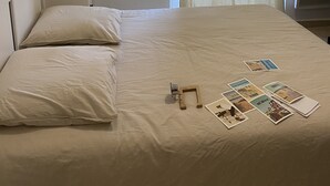 Una cama bien tendida con almohadas, una mesita de noche con lámpara, un cuadro colgado en la pared y una ventana con cortinas.