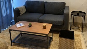 Un salón con un sofá gris, una mesa de centro de madera, una mesita auxiliar y una lámpara de pie.