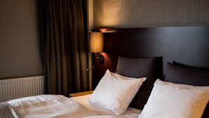 A hotel room with a neatly made bed, a headboard with a light fixture, and a window with curtains. - KRS LIVE Hotel (Kristiansand)