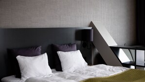 A modern hotel room with a bed, two pillows, a bedside table, a lamp, and a geometric-patterned wall. - KRS LIVE Hotel (Kristiansand)
