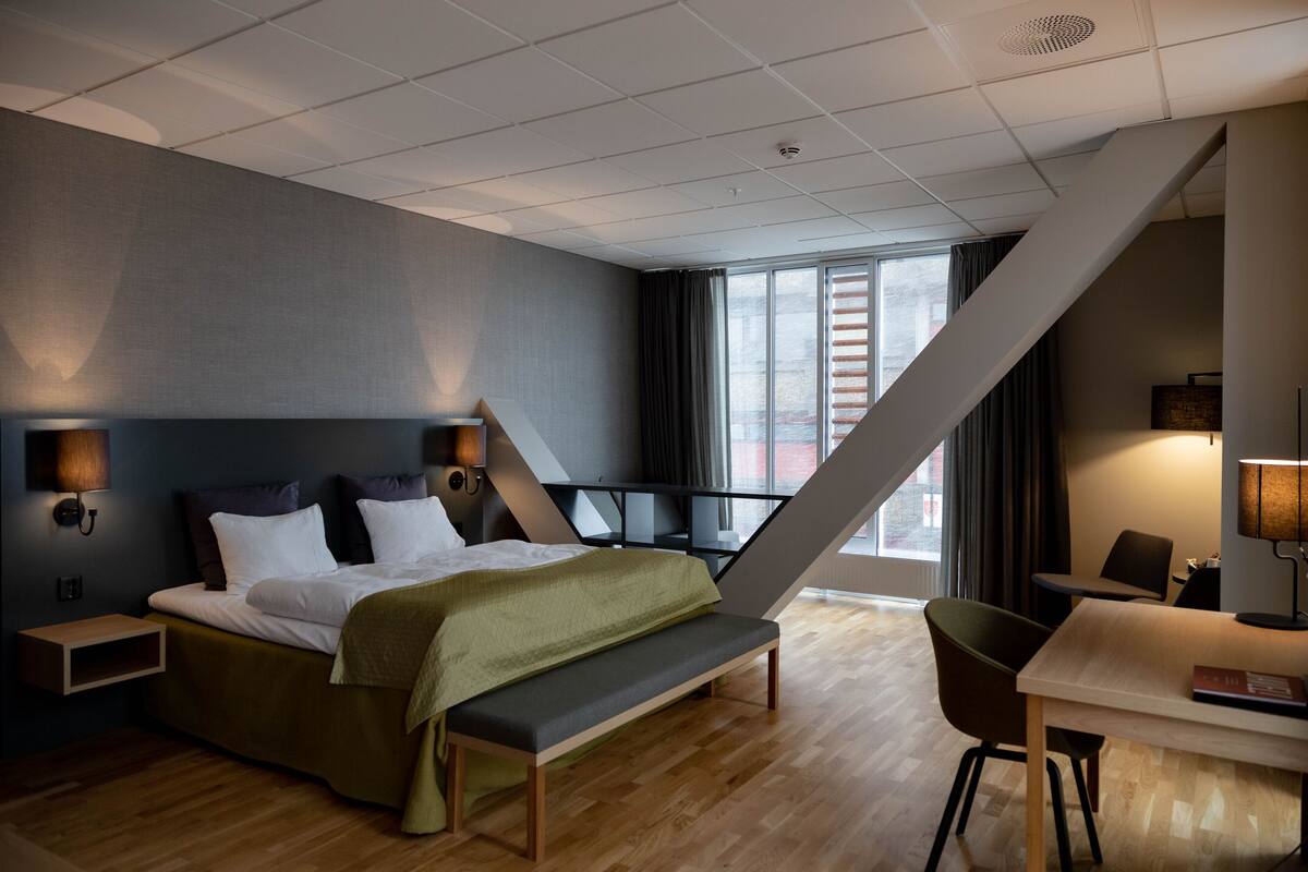 A modern hotel room with a bed, bench, desk, and chair.