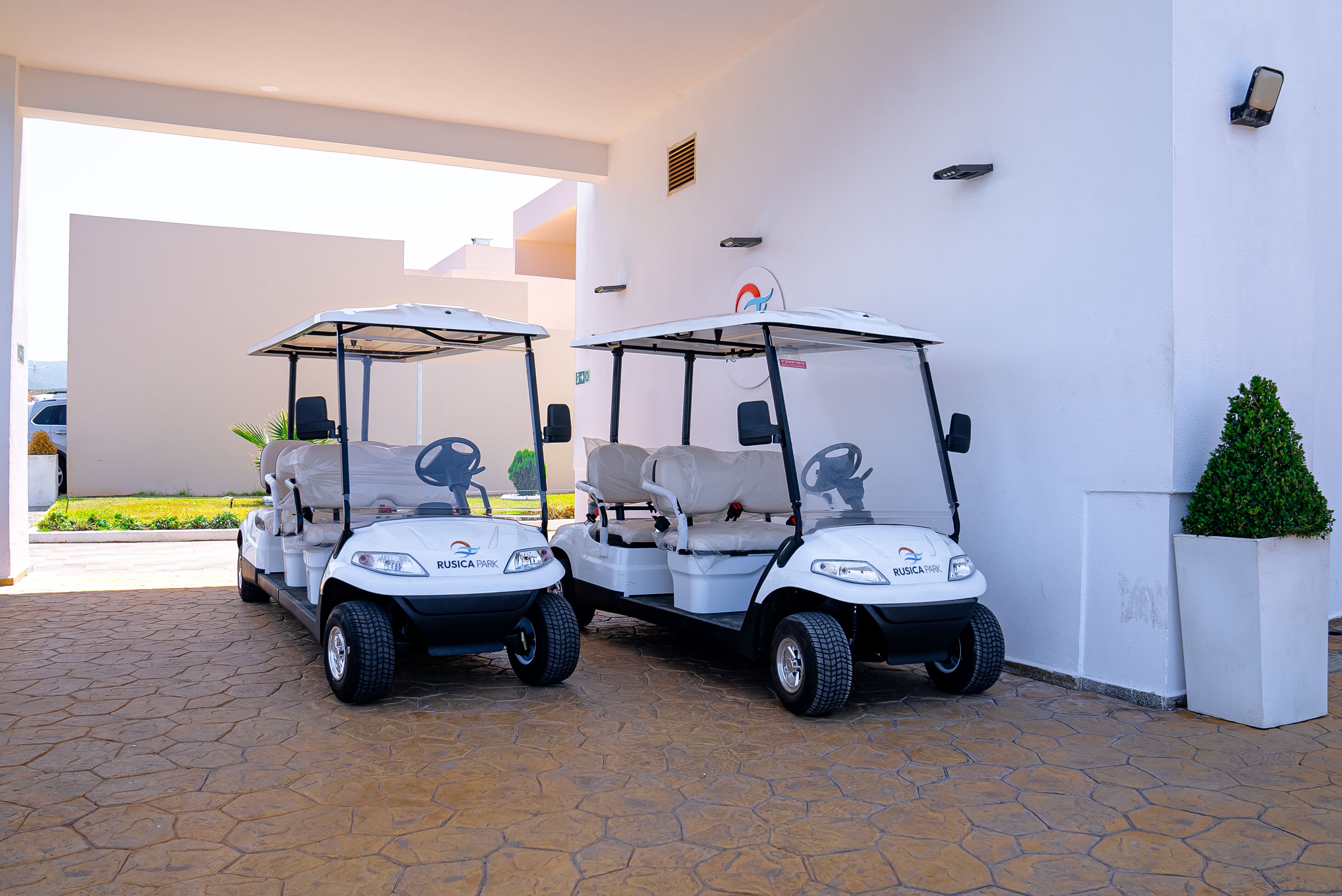 Dos carritos de golf estacionados frente a un edificio de diseño moderno, una planta en maceta y una vista despejada de la entrada.