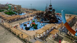 Un parque acuático con múltiples toboganes y atracciones, rodeado de asientos y sombrillas en la playa.