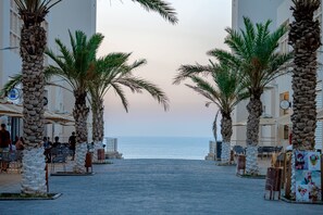 A paved walkway flanked by palm trees leading to a beach. - Rusica park  (Filfila)
