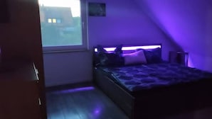 A bedroom with a bed, a window, and a purple light.
