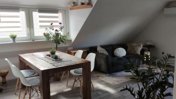 A dining area with a wooden table and chairs, a black sofa, and a window with blinds.