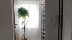 A hallway with a wooden floor, a white rug, a potted plant, a white chair, and a black framed picture on the wall.