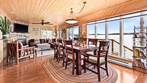 A spacious dining area with a wooden table and chairs, a fireplace, and large windows offering a view of the water. - Water's Edge on Lake Vermilion  (Tower)
