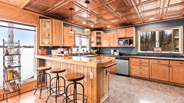 A kitchen with wooden cabinets, a central island with stools, and pendant lighting. - Water's Edge on Lake Vermilion  (Tower)