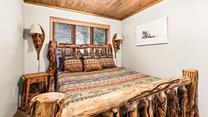 A bedroom with a wooden headboard, a patterned bedspread, and a window with blinds. - Water's Edge on Lake Vermilion  (Tower)