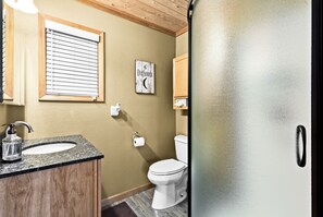 Une salle de bain avec un meuble-lavabo en bois, un évier, des toilettes et une porte en verre dépoli.