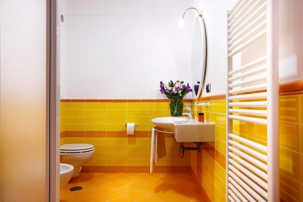 A bathroom with yellow tiles, a white toilet, a sink, and a mirror.