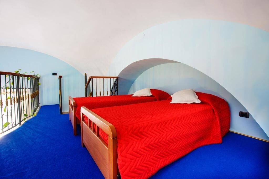 A bedroom with two beds, a blue carpet, and a balcony with a metal railing.