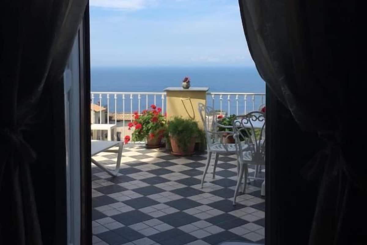 A balcony with a checkered floor, potted plants, and outdoor furniture.