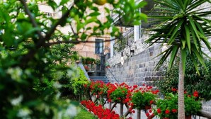 A narrow stone pathway flanked by red flowers and greenery, leading to a building with a metal gate and steps.