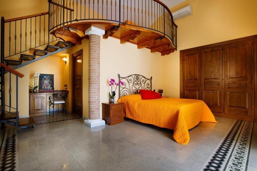 A bedroom with a bed, a nightstand, a dresser, a chair, a staircase, and a large wooden wardrobe.