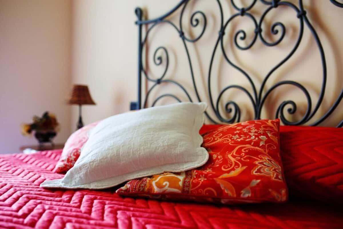 A bed with a red quilt, a white pillow, and a red patterned pillow.