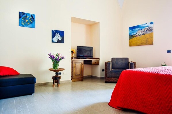A hotel room with a bed, a desk with a television, a chair, and artwork on the walls. - Relais Il Pennino (Massa Lubrense)