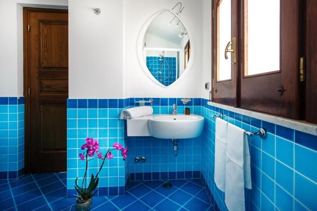 A bathroom with blue tiles, a white sink, a mirror, and a wooden door.