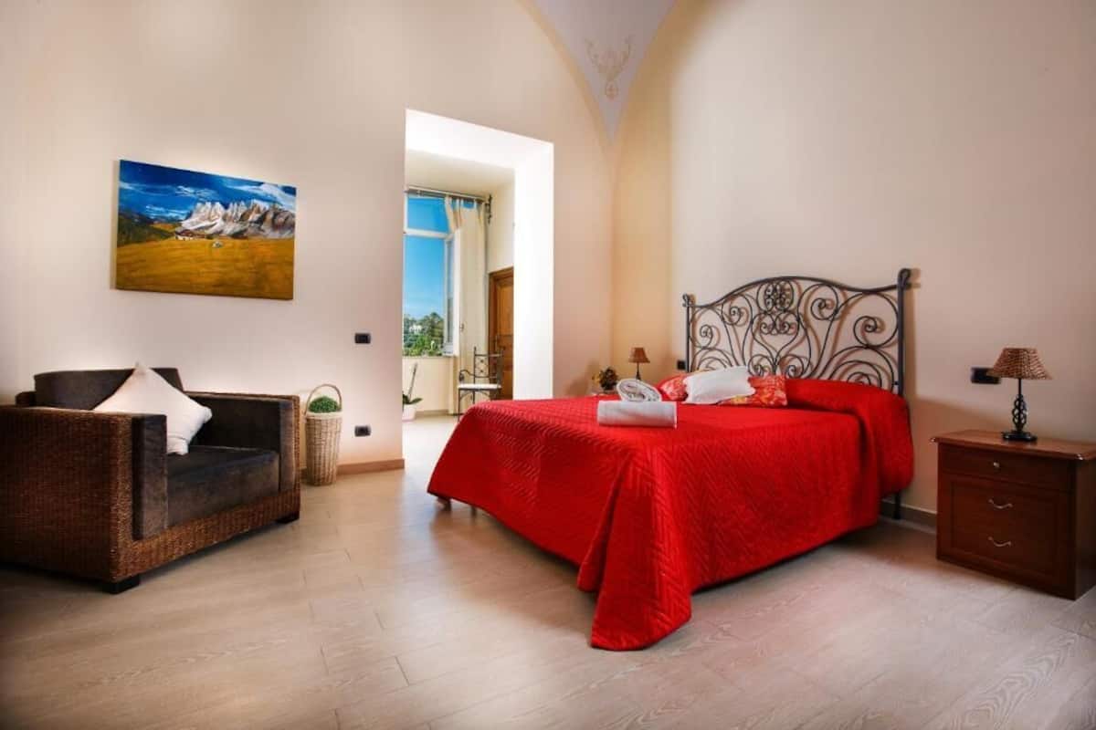 A bedroom with a bed, a sofa, a nightstand, and a painting on the wall.