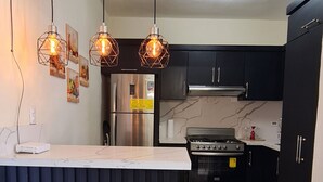 A modern kitchen with a central island, black cabinets, stainless steel appliances, and pendant lighting. - Central Apartment Facing the sea (Puerto Plata)