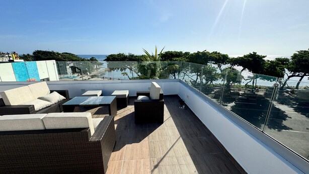 A rooftop terrace with outdoor seating, a glass balustrade, and a view of the sea. - Central Apartment Facing the sea (Puerto Plata)