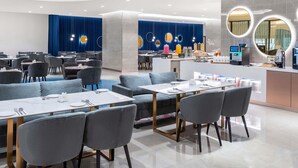 Ein modernes Restaurant mit runden Tischen und grauen Stühlen, einer Theke mit einer Kaffeemaschine und blauen Vorhängen im Hintergrund.
