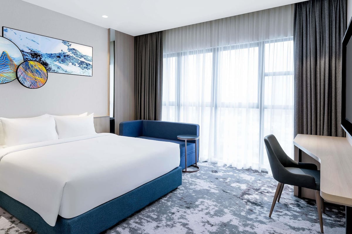 A hotel room with a bed, a desk, a chair, and a large window with curtains.