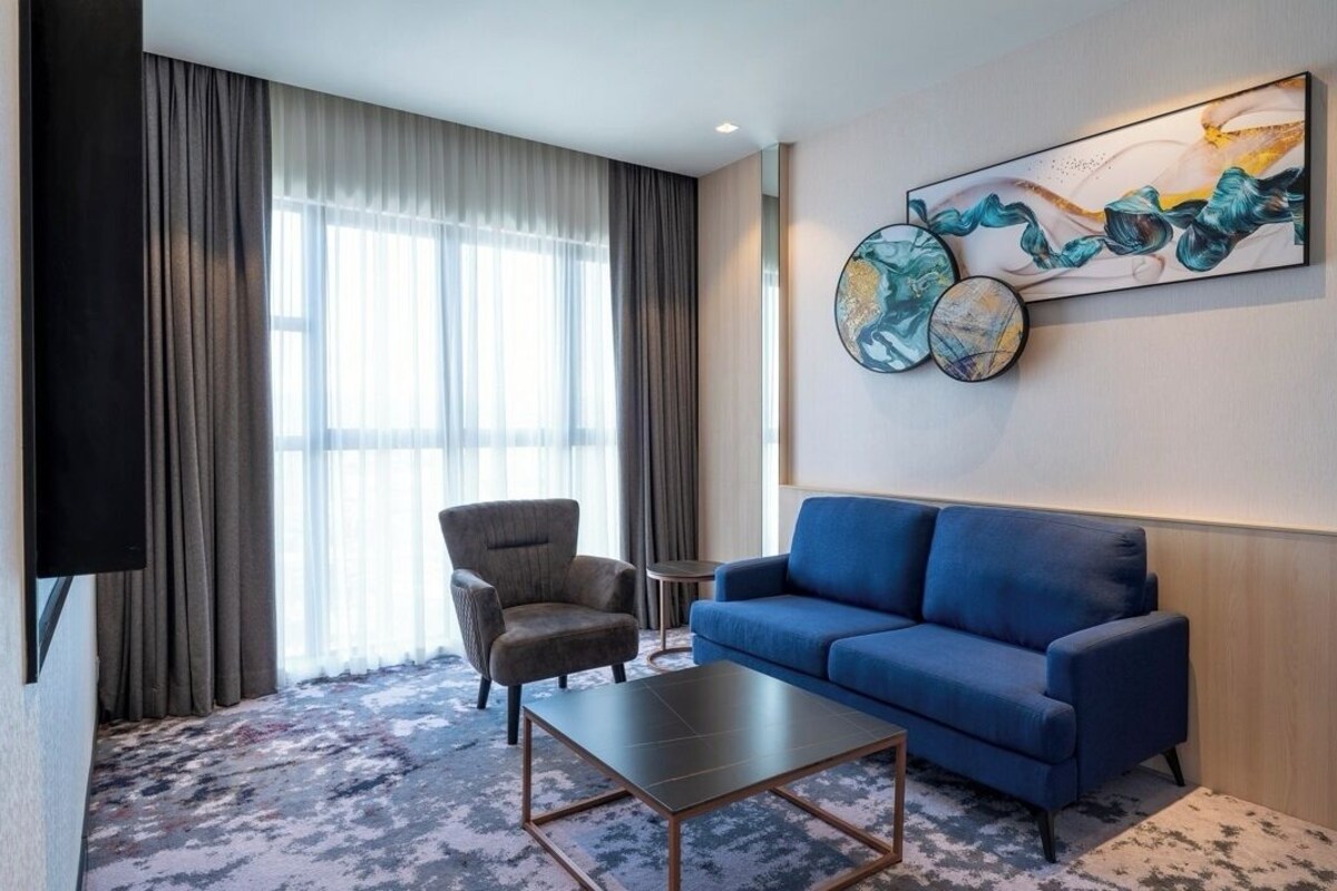 A hotel room with a blue sofa, a grey armchair, a small round table, and a flat-screen TV.