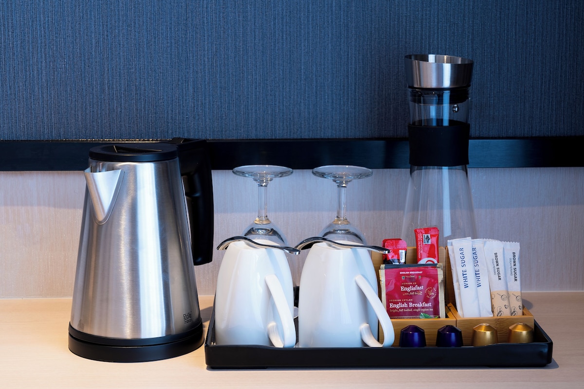 A coffee maker, two glass carafes, and a tray with sugar packets and creamer on a countertop.