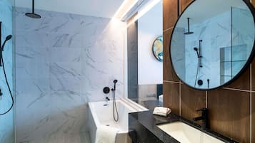 A modern bathroom with a marble floor, a bathtub, a sink with a black countertop, and a round mirror.