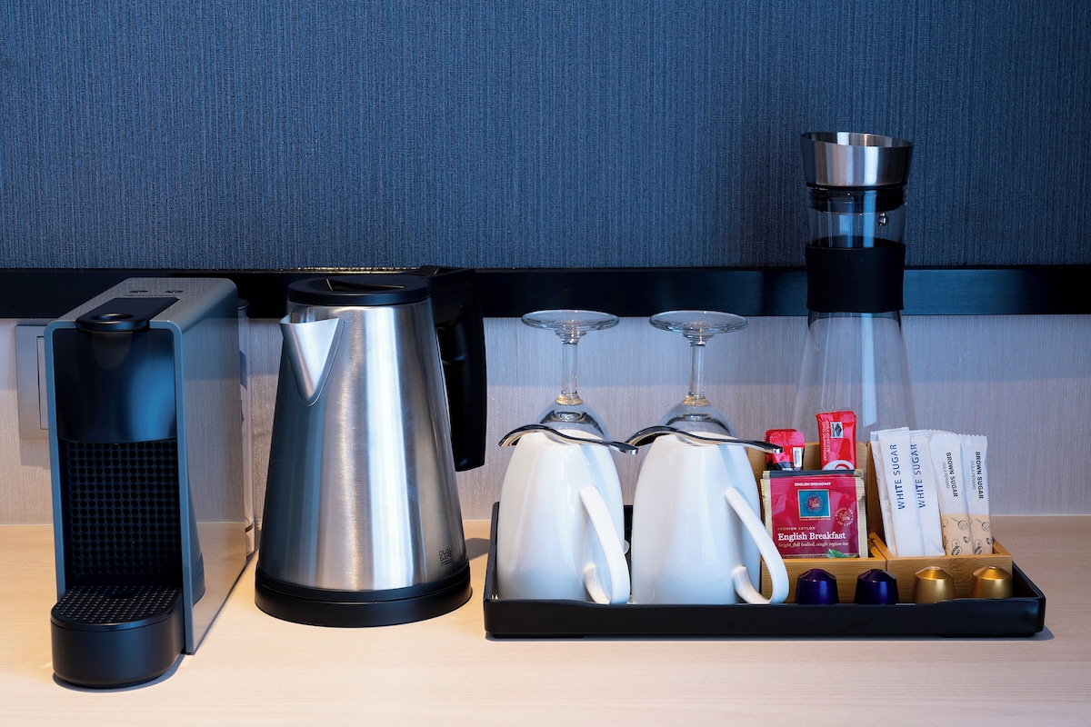 A coffee maker, a kettle, and a tray with sugar packets and a coffee grinder on a countertop.