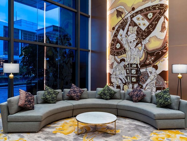 A modern lobby with a curved grey sofa, patterned cushions, a round coffee table, and a large wall mural. - Mercure Kuala Lumpur Trion (Kuala Lumpur)