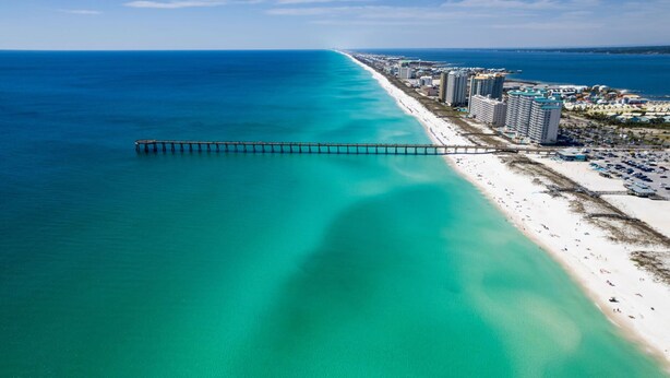 An aerial view of a coastal area with a long pier extending into the turquoise waters, adjacent to a sandy beach lined with high-rise buildings and a parking lot. - One of a kind Romantic Luxe Retreat, 8 Minutes to Emerald Beach, Outdoor Haven (Navarre)