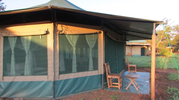 A tent with a covered porch, two wooden chairs, and a small table.