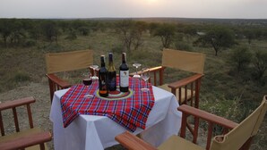 A table set outdoors with a plaid tablecloth, wine bottles, and glasses, surrounded by wooden chairs. - Osero Serengeti Luxury Tented Camp (Serengeti)