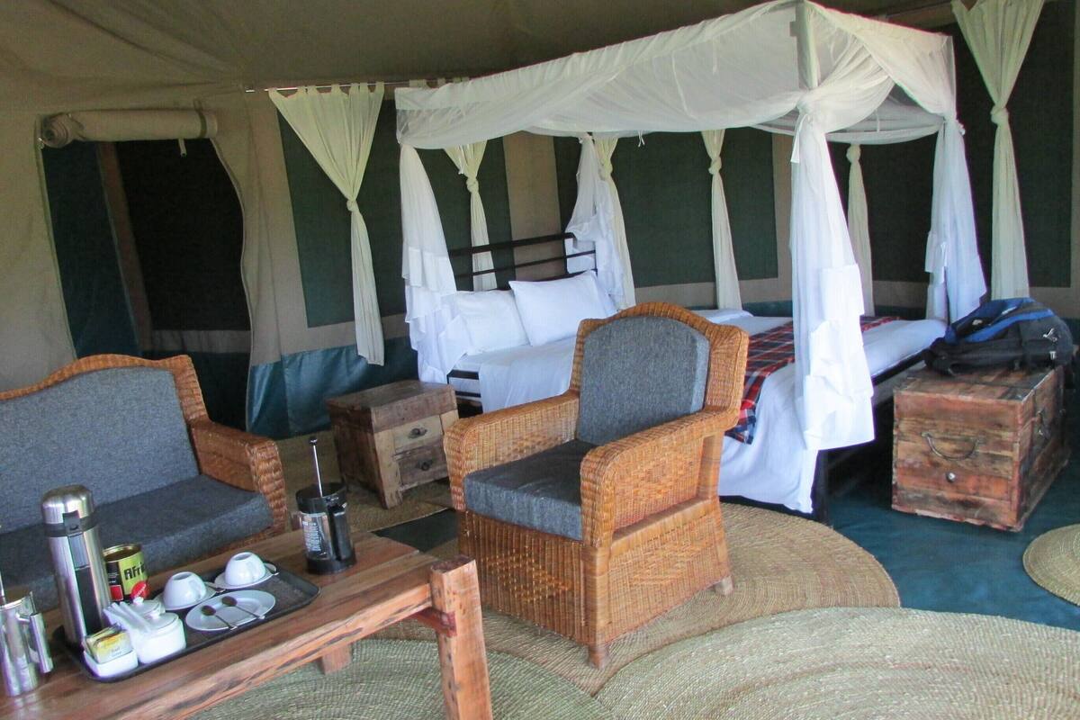 A tented accommodation with a bed, two sofas, a table with tea and utensils, and a suitcase.
