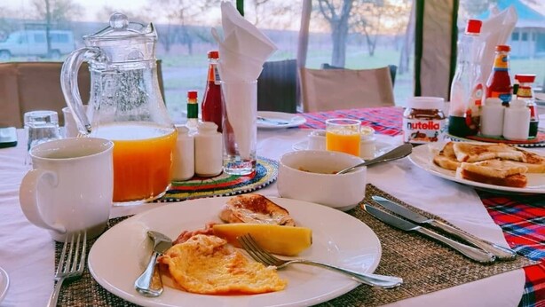 A breakfast table with a pitcher, cups, and plates of food. - Osero Serengeti Luxury Tented Camp (Serengeti)