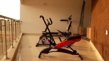 Un gimnasio con equipo de ejercicio, barandilla de vidrio y pared de madera.