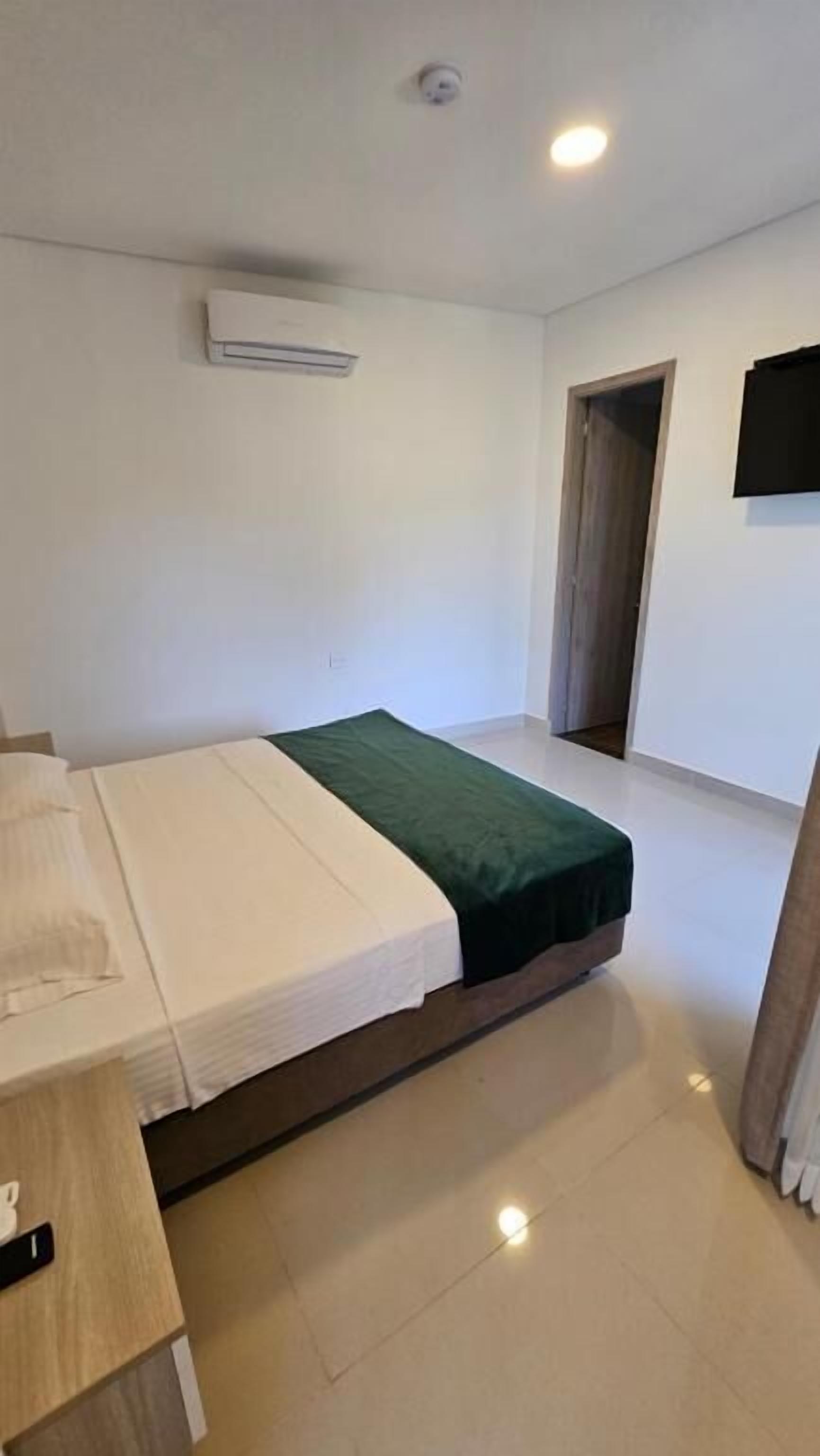 Quarto pequeno e limpo com uma cama, uma escrivaninha e uma televisão de tela plana na parede.