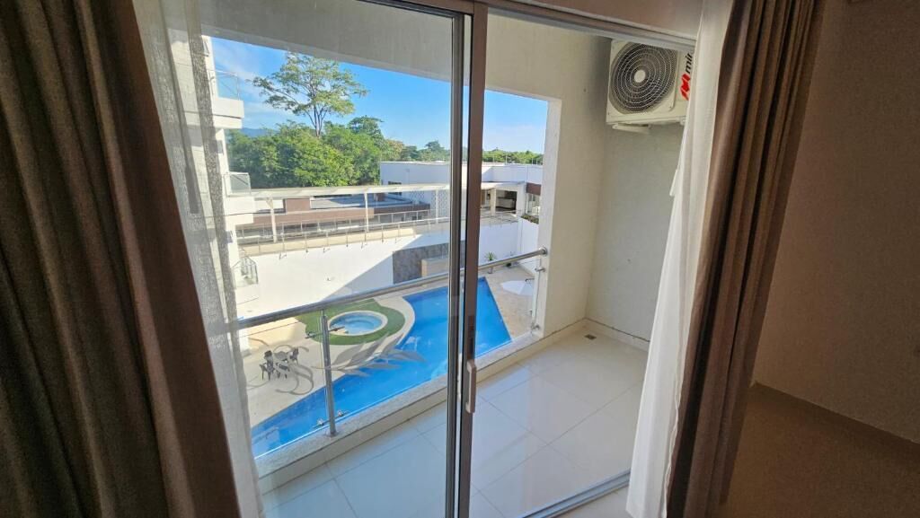 A balcony with a view of a swimming pool and a building with a rooftop garden.
