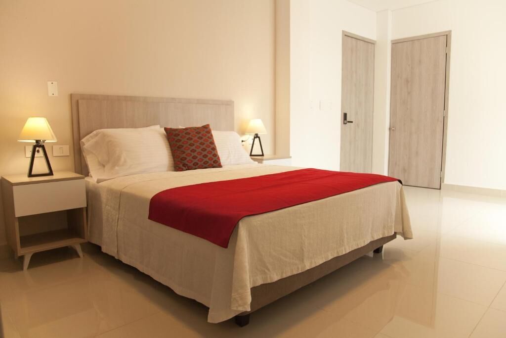 A neatly made bed with a red blanket, two bedside lamps, and a wooden headboard.